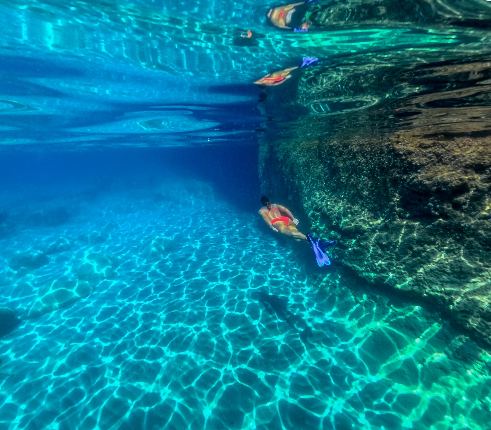 Swimmer exploring clear water beside a submerged rock wall